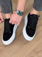 Crne kožne patike sa belim đonom u kadru sa rukom modela i sivom narukvicom sata