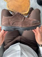 Muške cipele braon boje od brušene kože, prikaz u rukama modela iznad pantalona