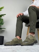 Model u beloj košulji sa maslinastim pantalonama i muškim cipelama maslinaste boje na fotelji