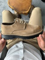 Muške cipele bež boje od brušene kože koje model pridržava iznad bež pantalona