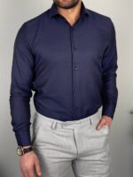 Teget elegantna muška košulja sa krem pantalonama u poslovnom ambijentu sa drvenim stočićem