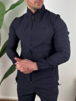Tri četvrt prikaz teget trenerka kompleta, model stoji opušteno uz biljku