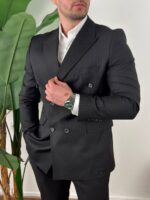 Pune dužine snimak crnog odela na pruge, model stoji bočno, ruka u džepu pantalona