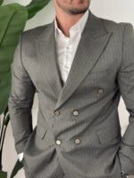 Model u maslinastom odelu na pruge sedi, sako otkopčan, vidljiv kroj pantalona